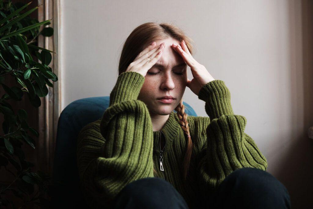 Adult female sitting with her fingertips on her forehead, possibly feeling nauseous, and wondering how long does Zofran stay in your system