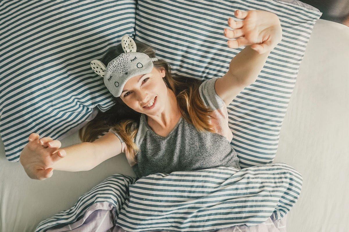 a young woman in mask for sleep stretches as she wakes up after using hot tub the night before