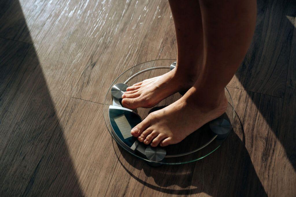 An adult pair of feet standing on some bathroom scales on a wooden floor depicting does glipizide cause weight gain?